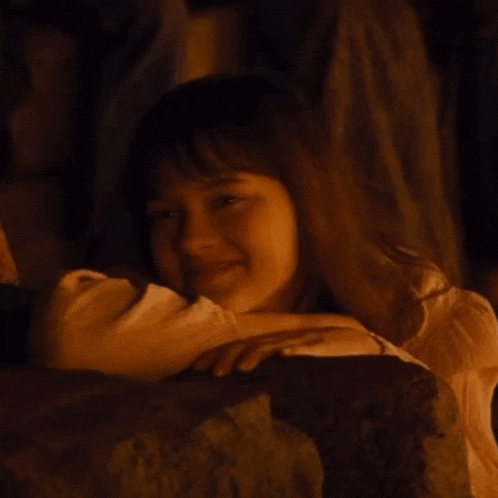 a young girl laying on a rock with her head on another person 's shoulder
