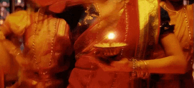 a woman in a red saree is holding a candle in her hand .