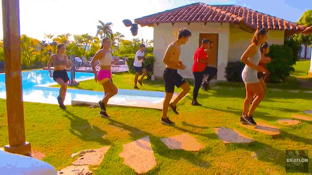 a group of people are running in front of a house that says exatlon on the bottom