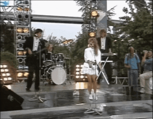 a woman singing into a microphone while a band plays behind her