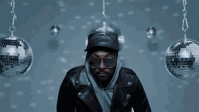 a man wearing sunglasses and a leather jacket is standing in front of disco balls