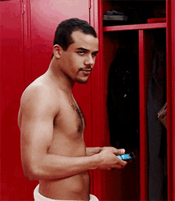 a shirtless man stands in front of a red locker