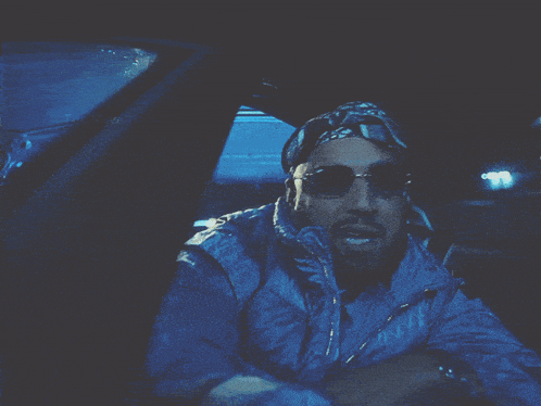 a man wearing sunglasses and a bandana is driving a car