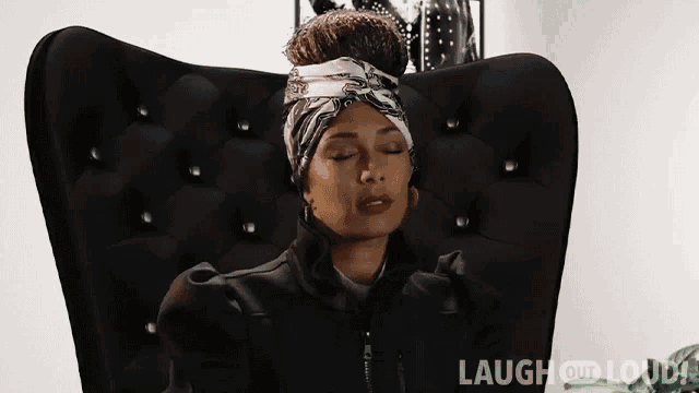 a woman is sitting in a black chair with her eyes closed and a bandana on her head .