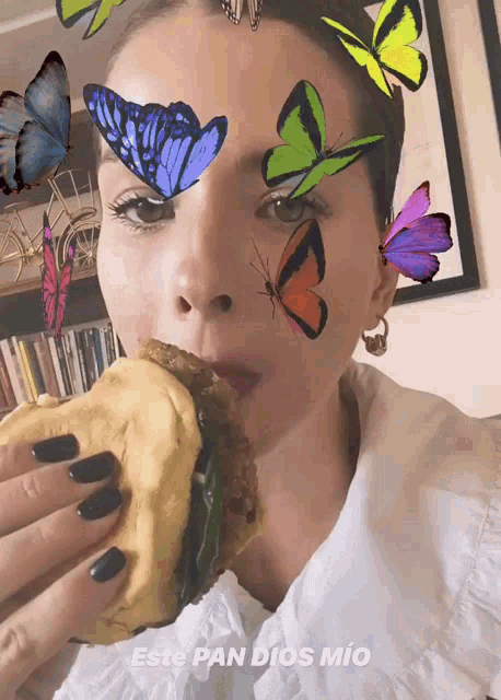 a woman is eating a sandwich with butterflies on her face and the words este pan dios mio below her