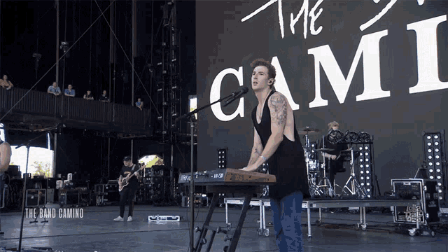 a man playing a keyboard in front of a sign that says " the band camino "