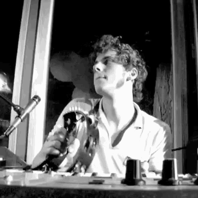 a man is sitting at a desk holding a microphone in front of a window in a black and white photo .