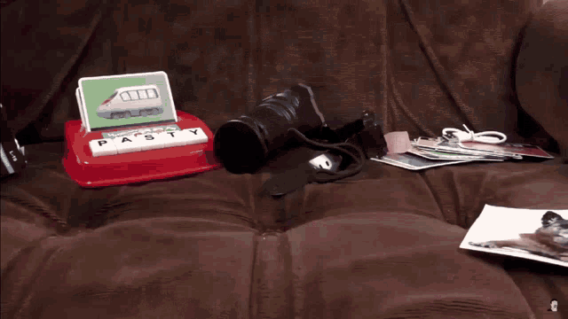 a camera sits on a brown couch next to a game that says pasty