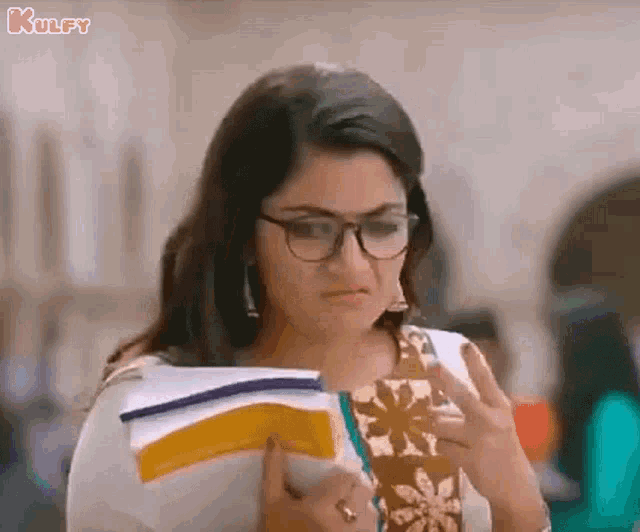 a woman wearing glasses is reading a book while holding a book .