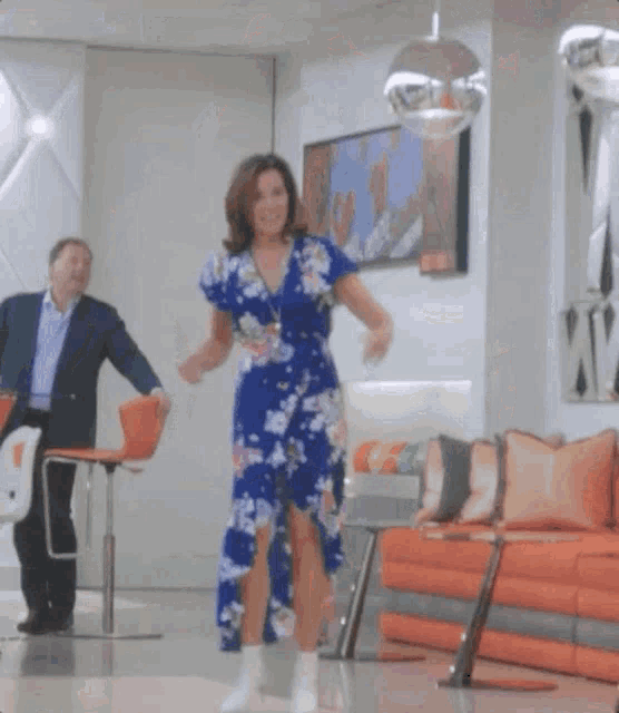 a woman in a blue floral dress is dancing with a man in a suit behind her