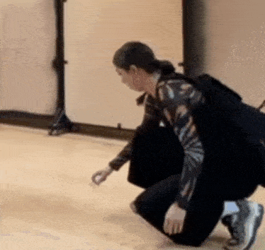 a woman is kneeling down on a wooden floor in a dance studio .