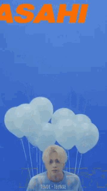 a man in a blue tie dye shirt is holding balloons in front of a blue background with the word asahi in orange