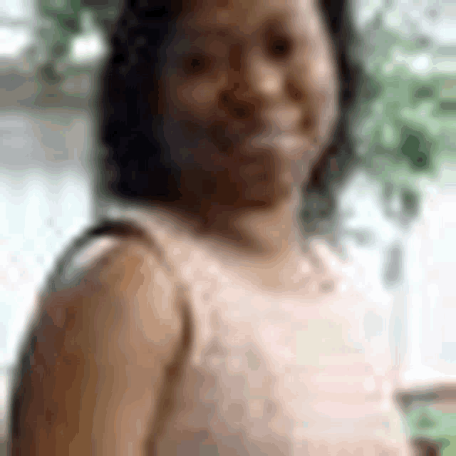 a woman in a pink tank top is smiling for the camera in a blurry photo .