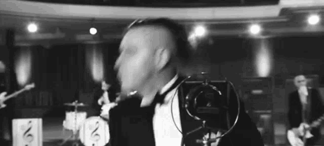a man in a tuxedo is singing into a microphone while a band plays behind him .