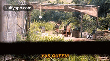 a group of people are sitting under a canopy in the woods and talking .