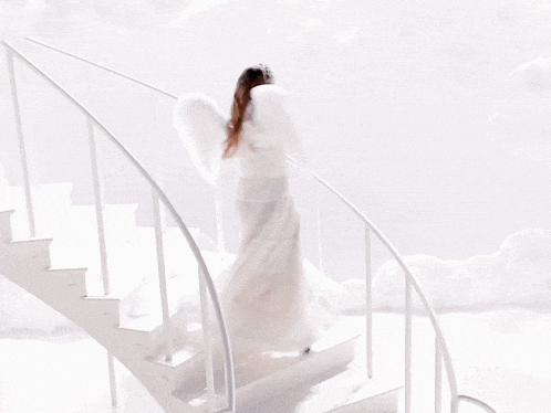 a woman in a white dress and angel wings is walking up a set of white stairs
