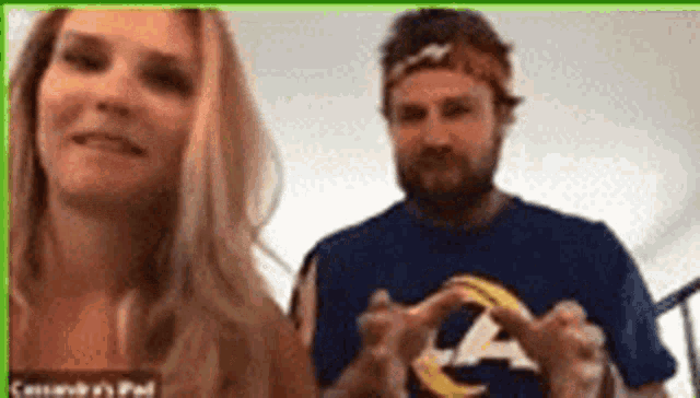 a man and a woman are making a heart shape with their hands in a video call .