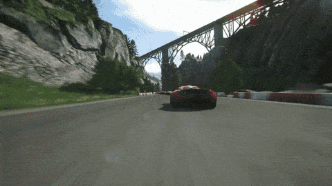 a red sports car is driving down a road with a bridge in the background