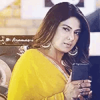 the woman is wearing a yellow saree and holding a cell phone .