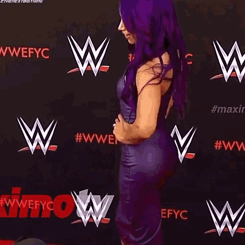 a woman in a purple dress is standing on a red carpet in front of a wall that says wwe on it .
