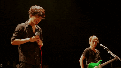 a man singing into a microphone next to a man playing a green guitar