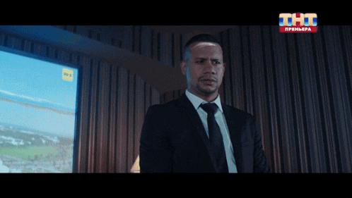 a man in a suit and tie stands in front of a tv screen that says tht premiere