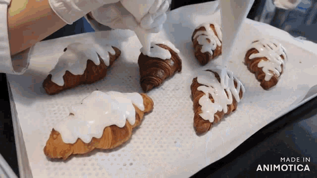 a bunch of croissants are being decorated with white frosting and the words made in animotica can be seen in the corner