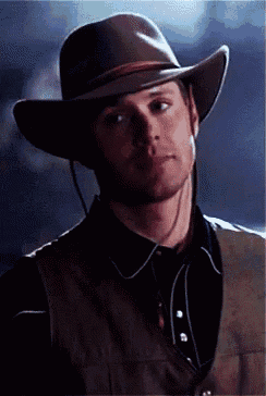 a man wearing a cowboy hat and vest looks to the side