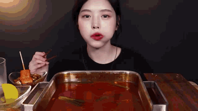 a woman is sitting at a table eating a tray of food with a fork .