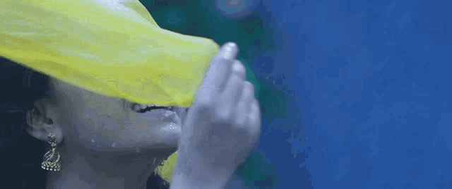 a woman covering her face with a yellow cloth in the rain