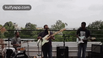 a man is playing a guitar and a drummer is playing drums on a rooftop .