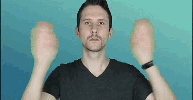 a man in a black shirt is holding his hands up in the air against a blue background .