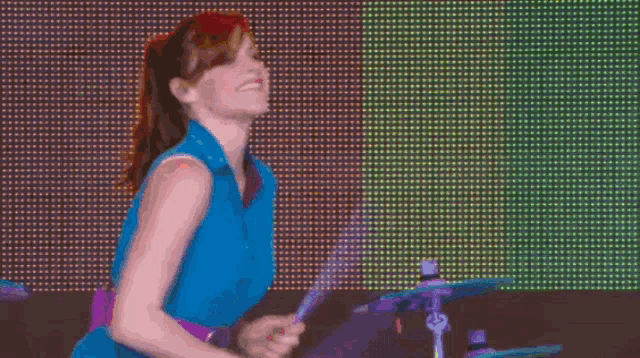 a woman in a blue shirt is playing drums in front of a large screen .