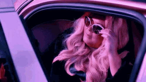 a woman wearing sunglasses is sitting in the back seat of a pink car .
