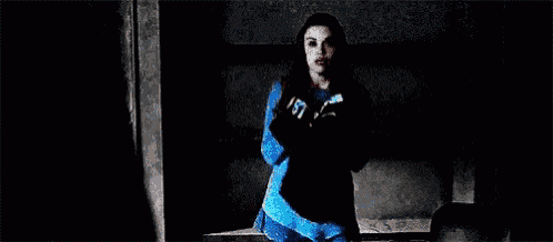 a woman is standing in a dark room wearing a blue jacket and black gloves .