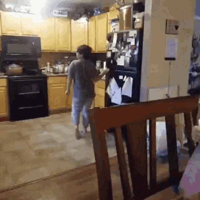 a woman standing in a kitchen with a black refrigerator and a microwave