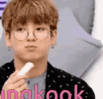 a young man wearing glasses and earrings is holding a stick in his hand with the word kook in the corner .