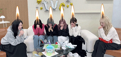 a group of young women are sitting on a couch with candles on their heads .
