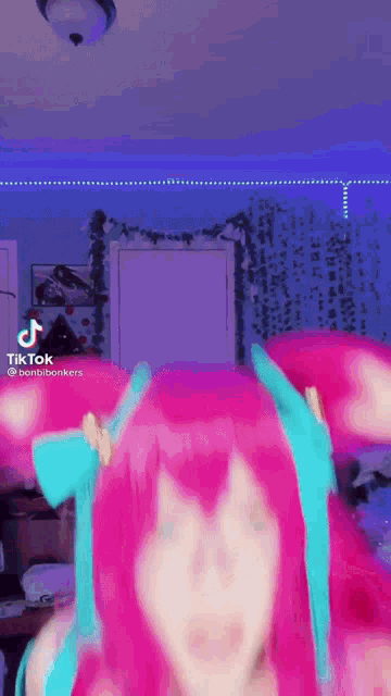 a woman with pink hair and blue ears is wearing a pink wig and a blue headband .