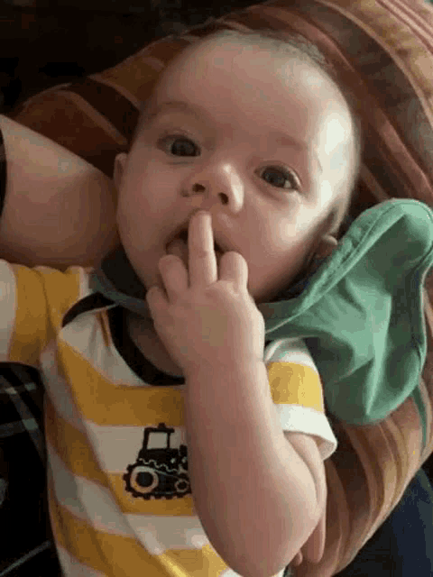a baby is laying on a couch and making a funny face while holding his finger to his mouth .