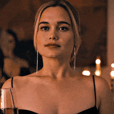 a woman in a black dress and earrings is holding a glass of wine