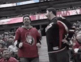 a couple of men are standing next to each other in a stadium . one of the men is wearing a spartans jersey .