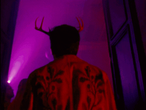 a man with antlers on his head is standing in front of a purple light