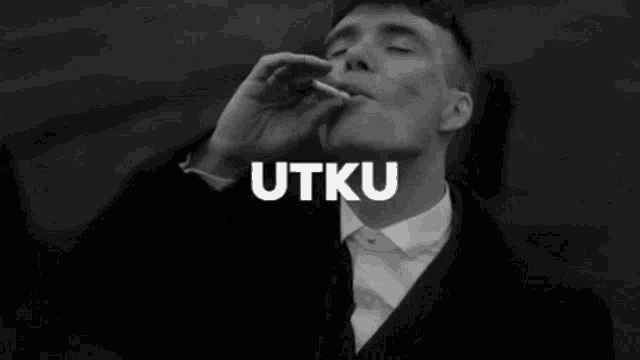 a man in a suit is smoking a cigarette and the word utku is above him