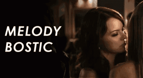 two women are kissing in a dark room with the words melody bostic behind them .