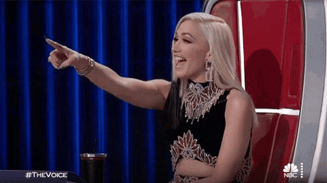 a woman in a black dress is pointing at something while sitting in a chair .