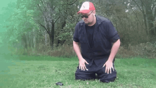 a man wearing a red hat and sunglasses is kneeling down in the grass