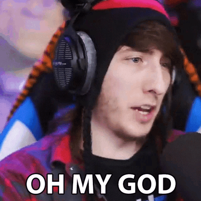a man wearing headphones and a hat is sitting in front of a microphone and saying oh my god .