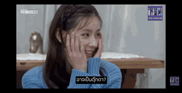 a girl in a blue sweater has her hands on her face and the words thai fanclub are on the bottom