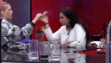 two women are sitting at a table with a pitcher of water and a blender .